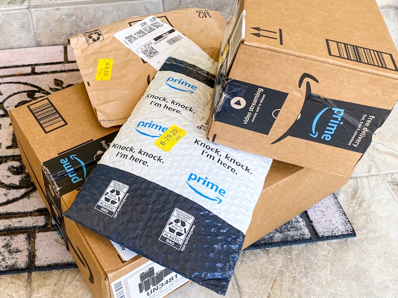 A pile of Amazon boxes and Amazon packing envelopes sitting on a doormat outside a front door.