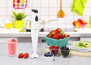 a hand blender on a counter with fruit and a smoothie