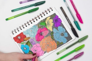 someone drawing flowers in a sketchbook with colorful gel pens