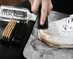 a shoe cleaner kit and a hand cleaning a sneaker