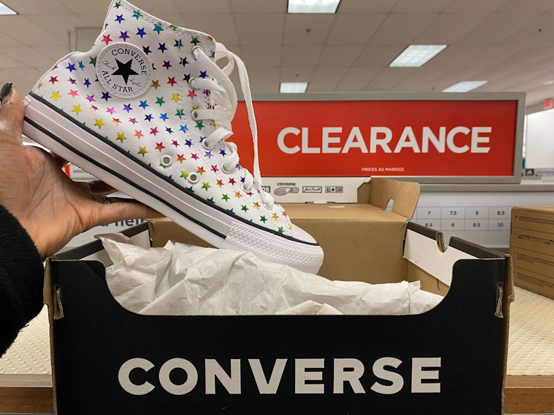 A person's hand holding up a Converse All-Star high-top shoe above its box on a clearance shelf at Kohl's.