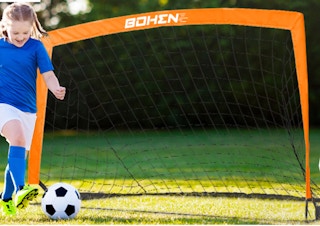 a girl kicking a soccer ball at an orange goal