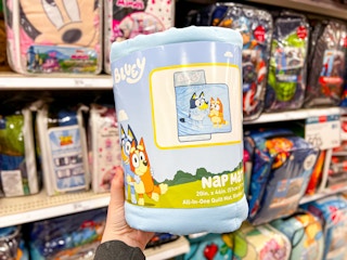 hand holding the Bluey nap mat in front of the character bedding at TArget