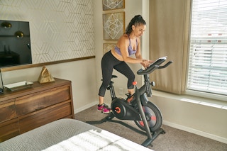 A woman using a stationary exercise bike in her room.