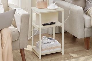 A cream-color end table sits between two upholstered chairs. Electronic items are plugged into the table.