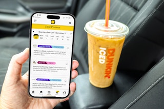 a person holding up the kcl app with a dunkin iced coffee in the background