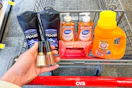 person holding 2 revlon nail polishes over a cart with axe body wash, dial soap, neutrogena wipes, and arm & hammer detergent in it