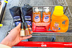 person holding 2 revlon nail polishes over a cart with axe body wash, dial soap, neutrogena wipes, and arm & hammer detergent in it