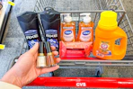 person holding 2 revlon nail polishes over a cart with axe body wash, dial soap, neutrogena wipes, and arm & hammer detergent in it