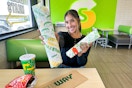 a woman holding out subway sandwiches
