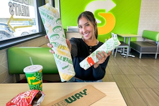 a woman holding out subway sandwiches