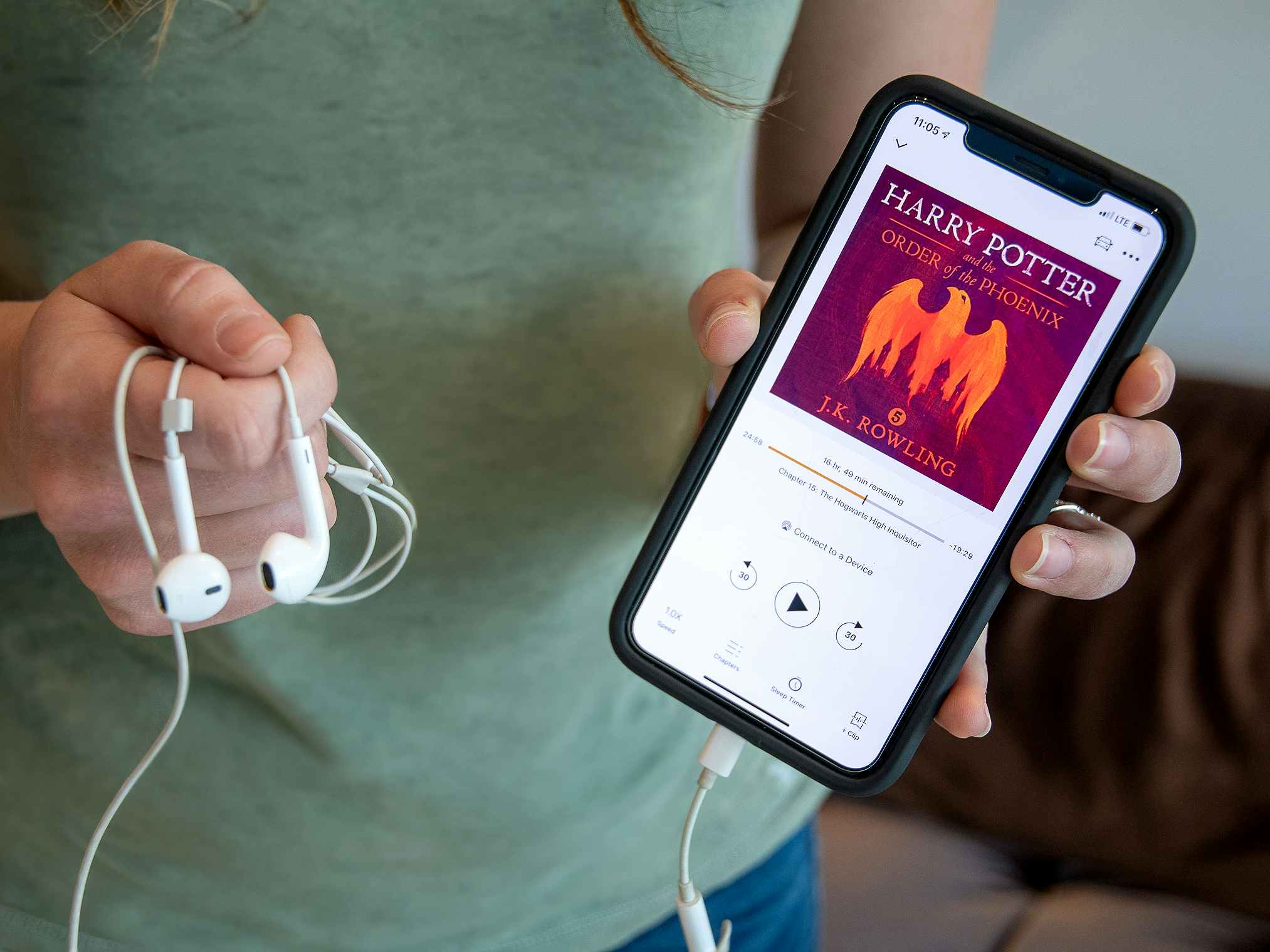 A person holding an iPhone and headphones with Harry Potter and the Order of the Phoenix from audible on the screen