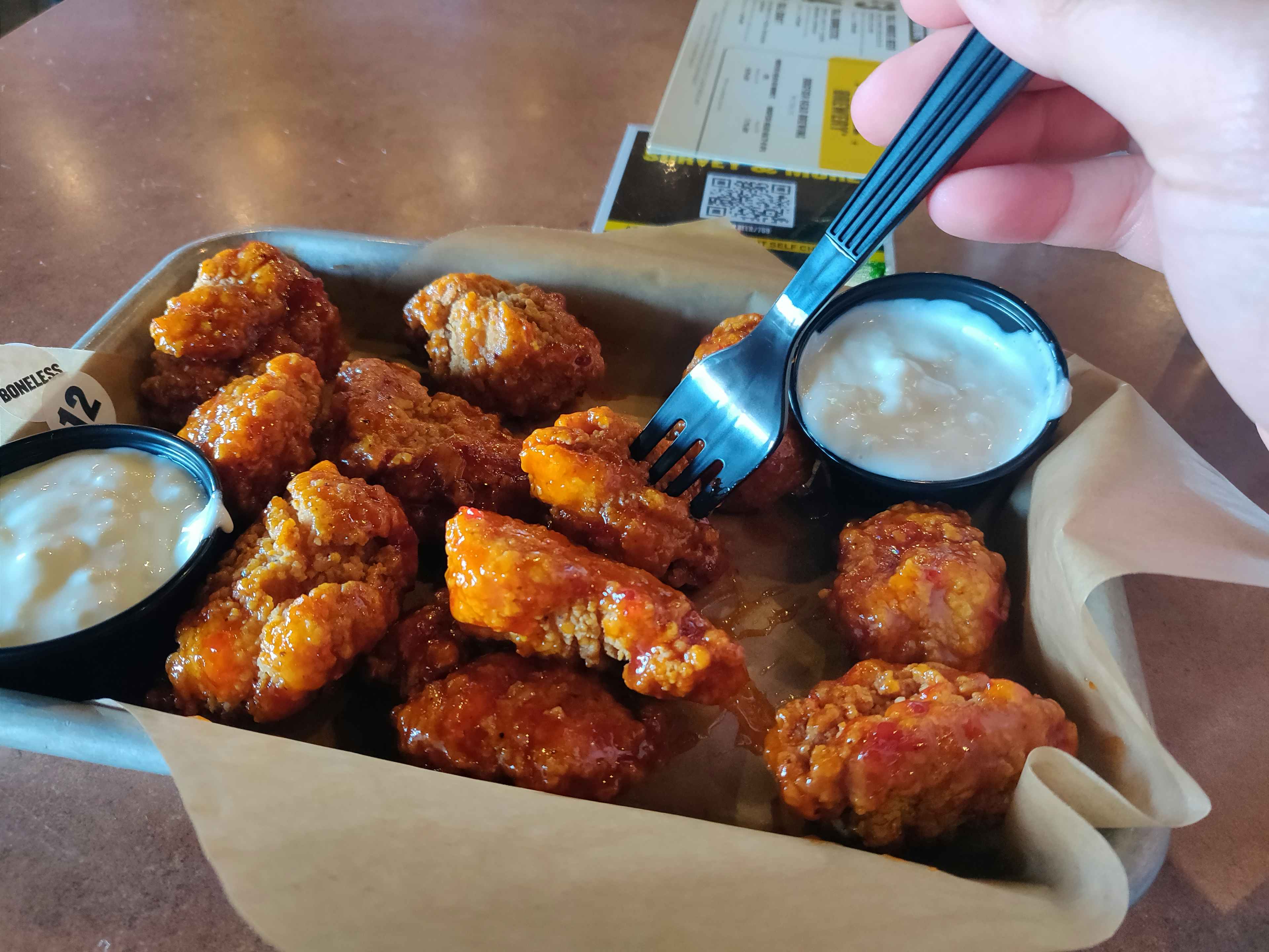 person putting their fork into buffalo wild wings boneless wings.