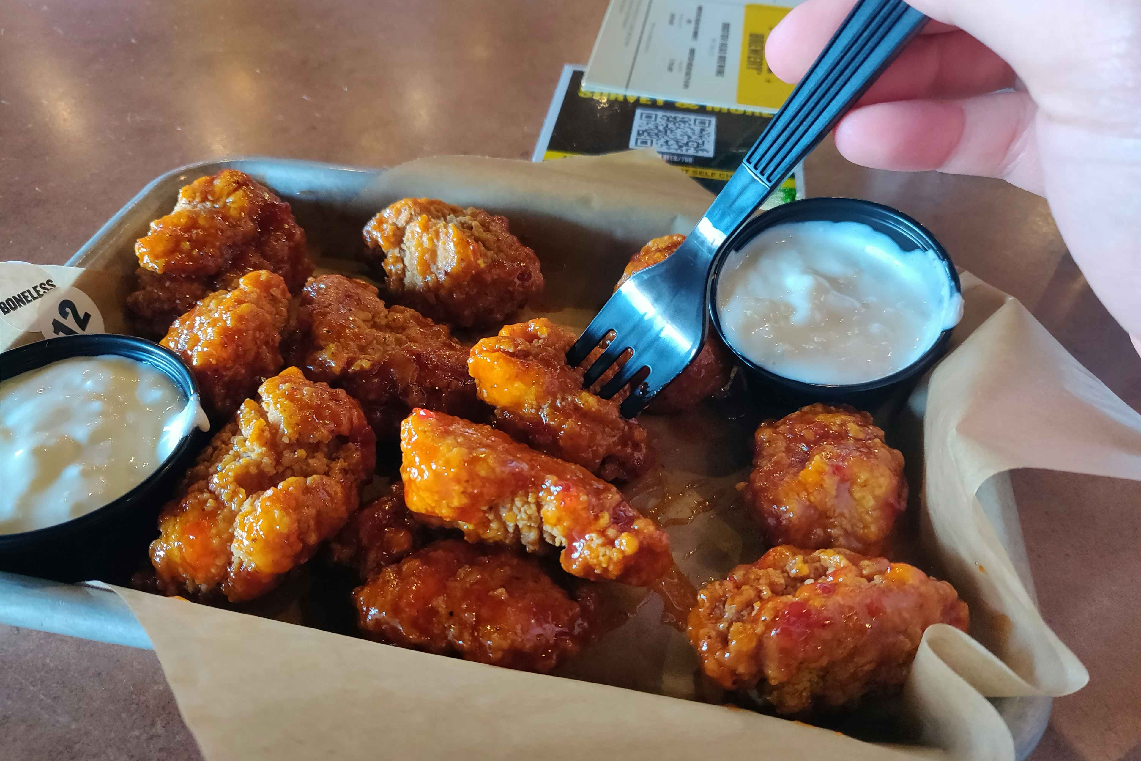 person putting their fork into buffalo wild wings boneless wings.