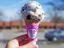 A person's hand holding up a Baskin Robbins ice cream cone.