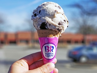 A person's hand holding up a Baskin Robbins ice cream cone.