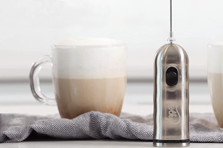 A milk frother on a table near a coffee.