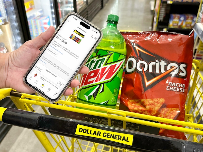 Someone holding up a phone displaying a digital coupon on the Dollar General app next to a cart with products