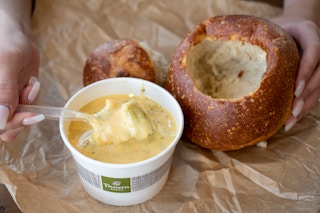 A cup of soup next to a bread bowl