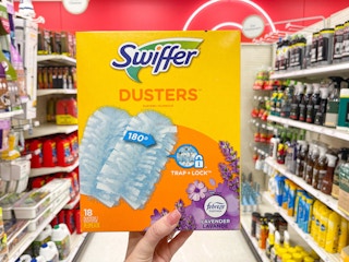 A Swiffer Dusters box held out in front of a store aisle, by hand.