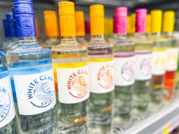 Hand holding a mango flavor of White Claw vodka in front of the White Claw Vodka shelf
