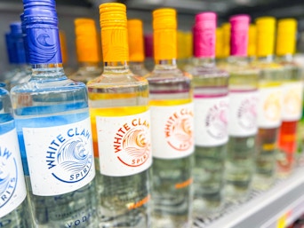 Hand holding a mango flavor of White Claw vodka in front of the White Claw Vodka shelf