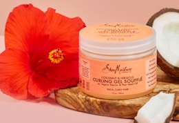 a pink jar of hair gel next to a coconut and a red flower