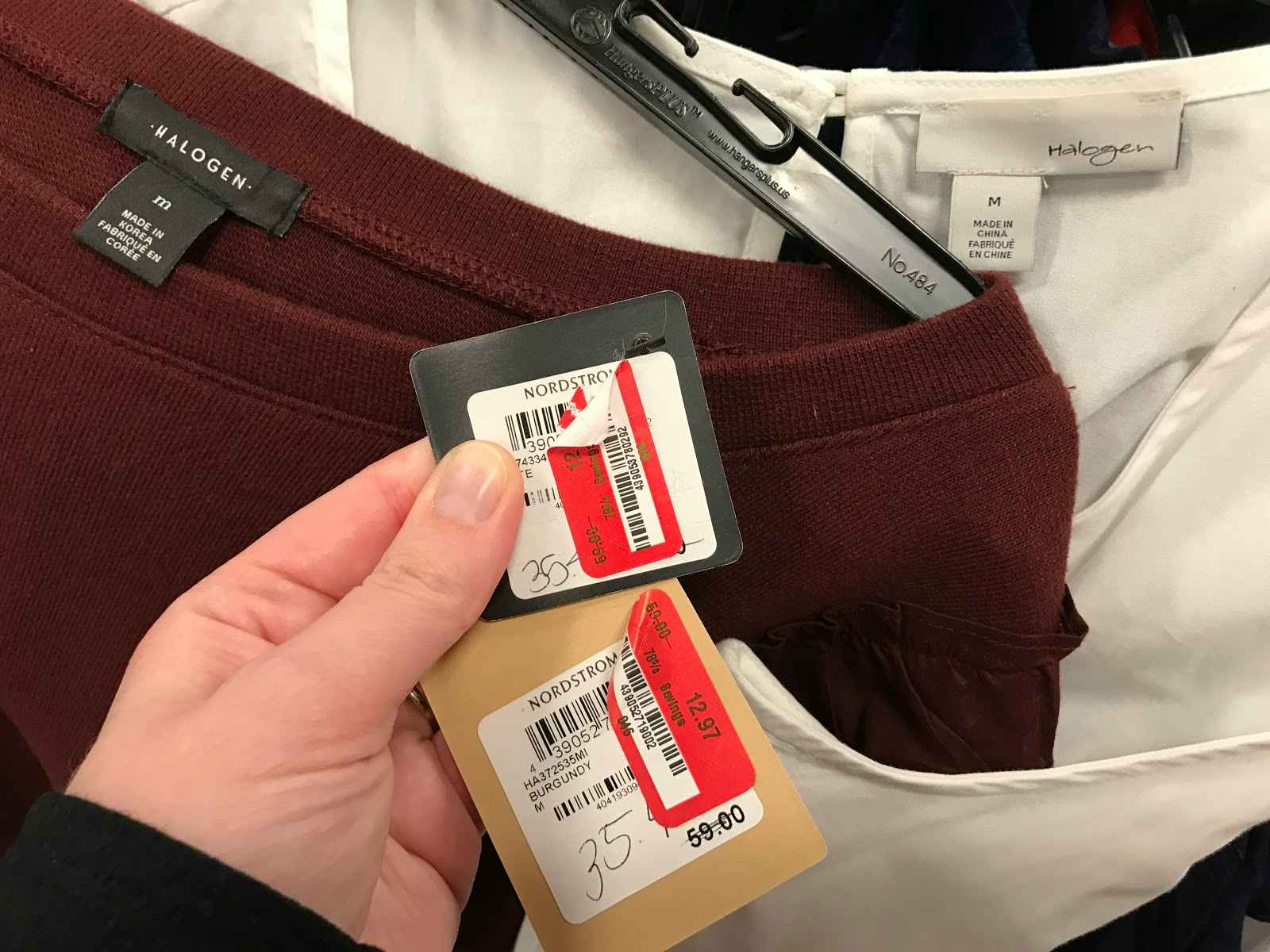 A person holding two price tags attached to clothing. Each tag has a red and white price sticker on it. Those stickers a peeled back to r...