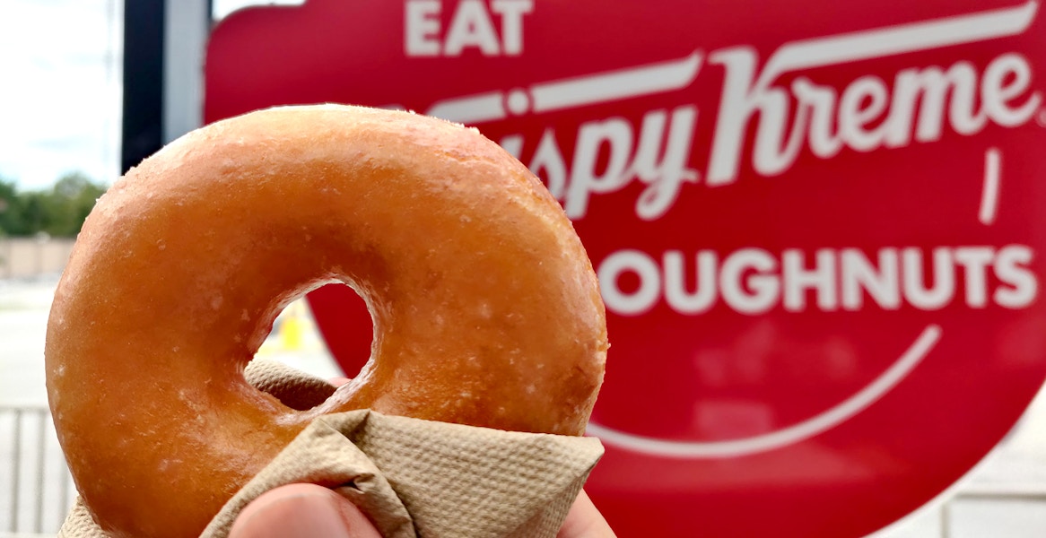 hand holding krispy kreme pumpkin spice donut near signage
