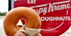 hand holding krispy kreme pumpkin spice donut near signage