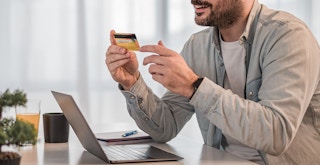 A person looking at a credit card while on a laptop
