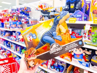 hand holding an imaginext jurassic world dinosaur in front of a target shelf