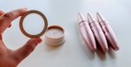 a person holding a cap to an empty blush with three tubes of mascara in the background