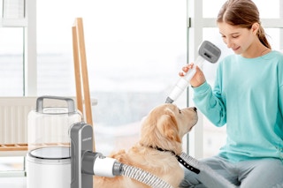 A young girl holds the pet grooming vac head as she smiles at her dog.