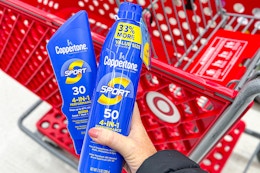 hand holding 2 coppertone sunscreen in front of a target cart