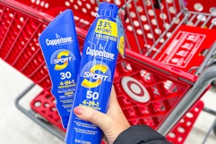 hand holding 2 coppertone sunscreen in front of a target cart