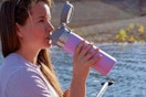 Woman sitting on a dock, drinking from the  Stanley Quick Flip GO Water Bottle 36 oz.