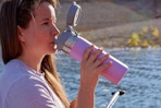 Woman sitting on a dock, drinking from the  Stanley Quick Flip GO Water Bottle 36 oz.