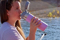 Woman sitting on a dock, drinking from the Stanley Quick Flip GO Water Bottle 36 oz.