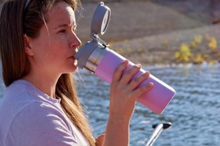 Woman sitting on a dock, drinking from the Stanley Quick Flip GO Water Bottle 36 oz.