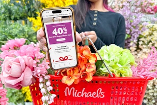 a person holding a michaels basket filled with faux flowers holding out a cellphone with a 40 off coupon on screen 