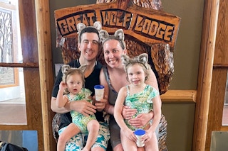 A family sitting together on a wooden bear seat at the entrance of Great Wolf Lodge