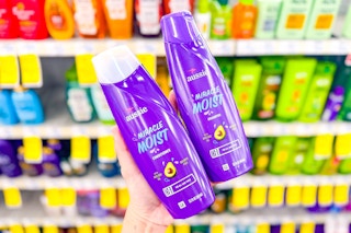 person holding aussie shampoo and conditioner in front of shelves