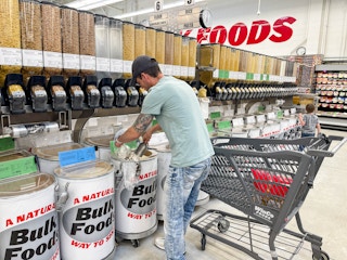 a man filling up a bag in the winco bulk foods area next to a cart