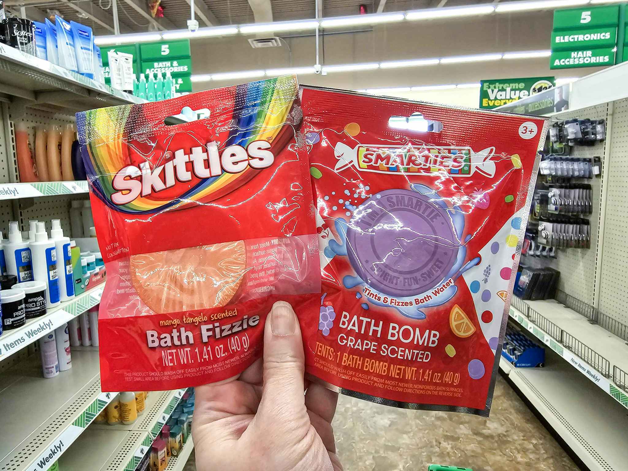 person holding skittles & smarties bath bombs in an aisle