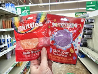 person holding skittles & smarties bath bombs in an aisle