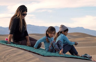 a mom and two kids sitting on an adventure blanket