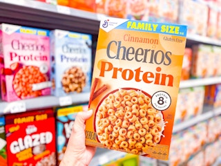 hand holding a box of cheerios protein cereal in walmart aisle