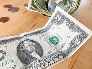 a two dollar bill with coin change in the background