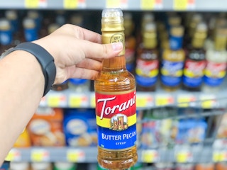 hand holding out Torani bottle in front of Walmart store shelf